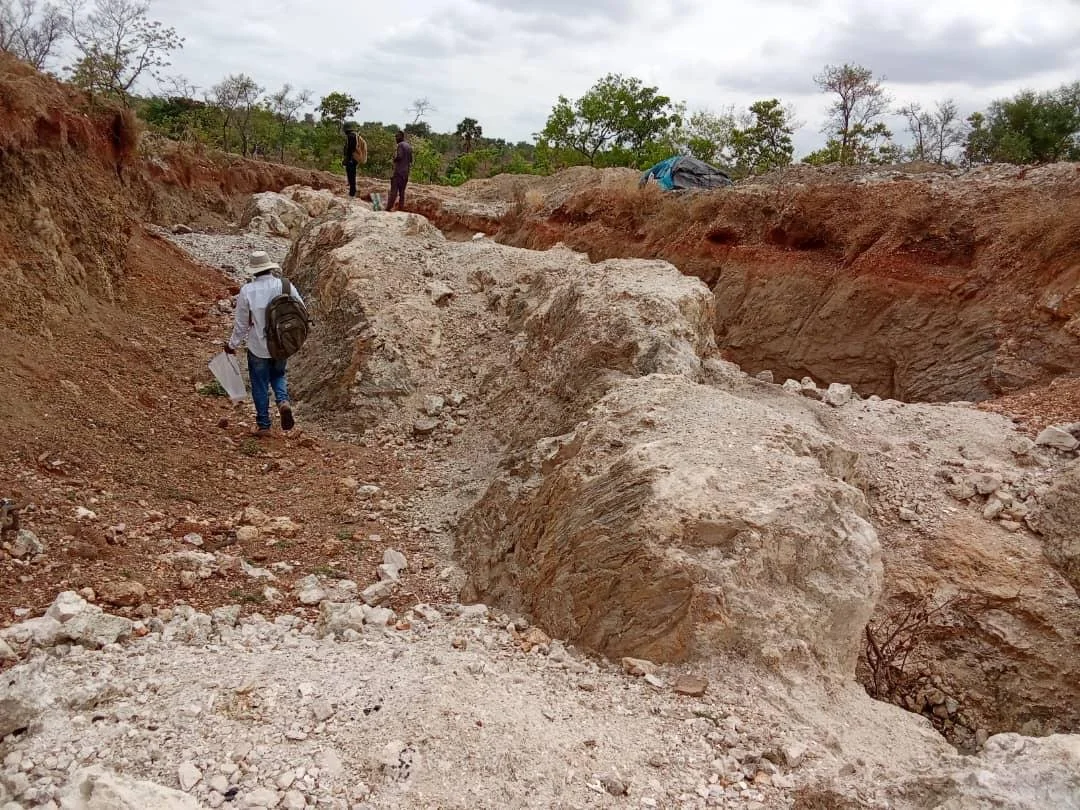 Geologists inspecting exposed rock and exploration trenches at an African project site